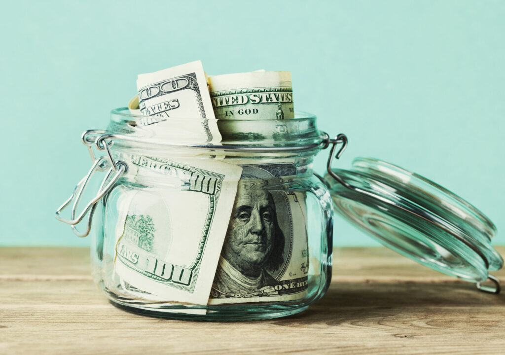 Dollar bills in glass jar on wooden table. Saving money concept
