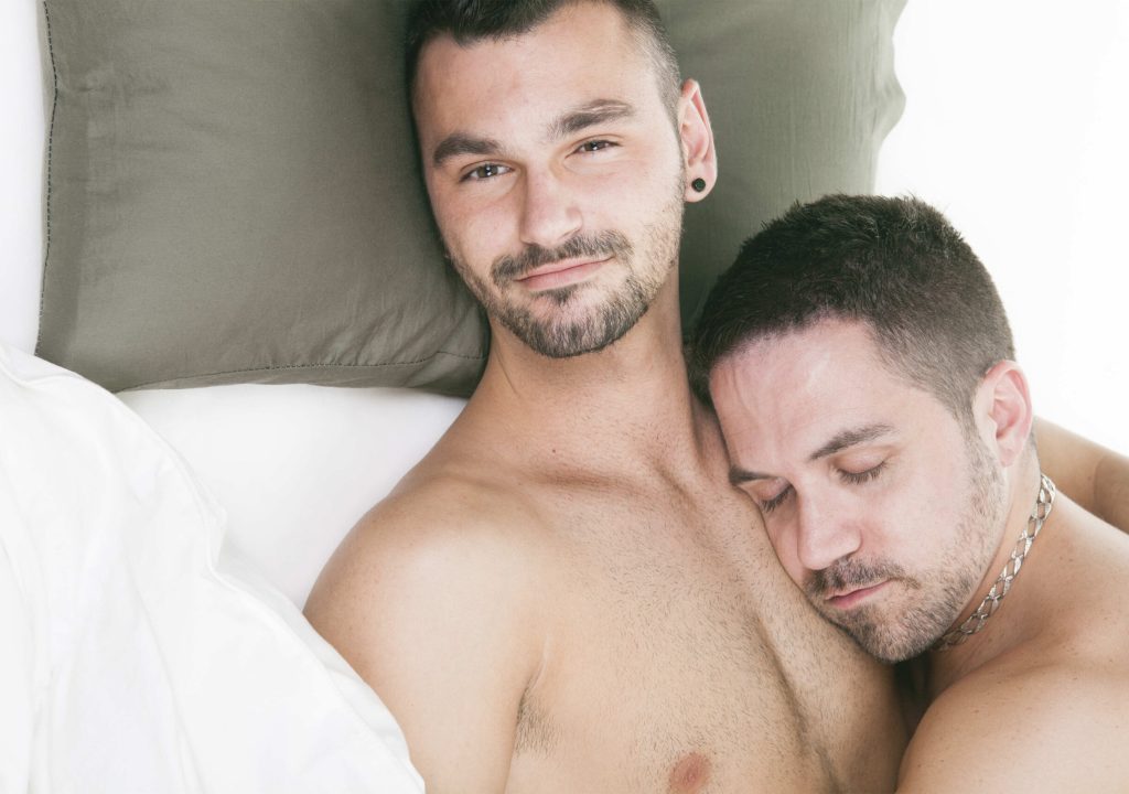 A homosexual couple onder a bed in studio white on studio.