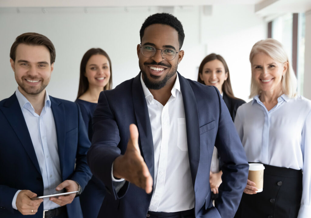 Portrait of smiling African American team leader stretch hand greeting job candidate or applicant in office. Happy multiracial businesspeople meet welcome newcomer at workplace. Employment concept.