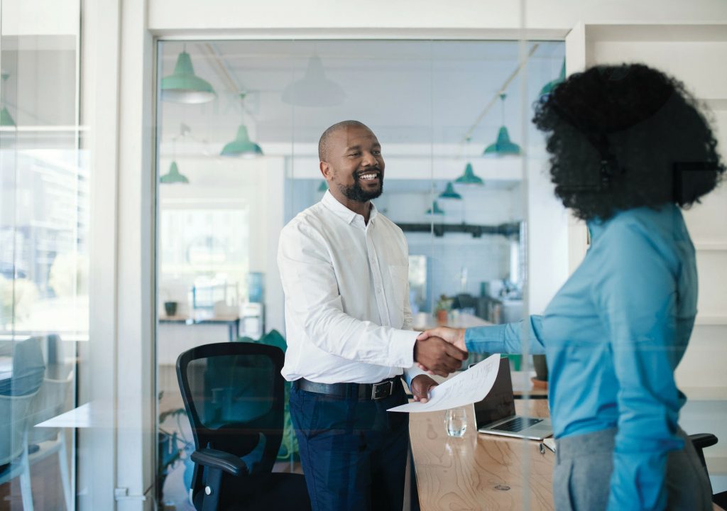 Smiling African American manager shaking hands with a new job applicant after an interview while standing together in his office
