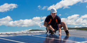 Solar panel technician with drill installing solar panels on roof on a sunny day
