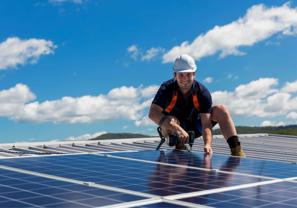 Solar panel technician with drill installing solar panels on roof on a sunny day