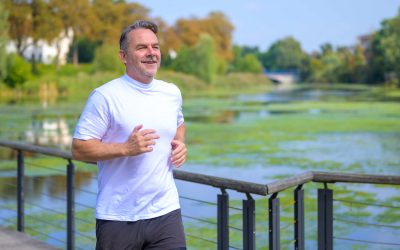 Sporty senior man jogging over a bridge over a river. Sporty senior man jogging over a bridge over a tranquil river in close up with copyspace in a health and fitness concept