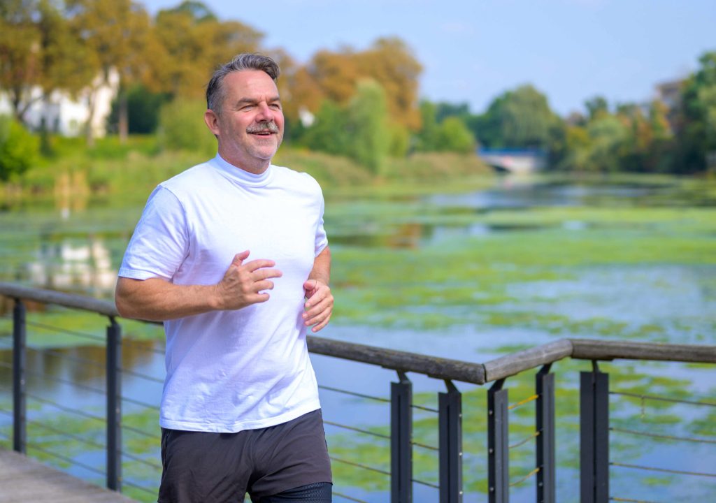 Sporty senior man jogging over a bridge over a river. Sporty senior man jogging over a bridge over a tranquil river in close up with copyspace in a health and fitness concept
