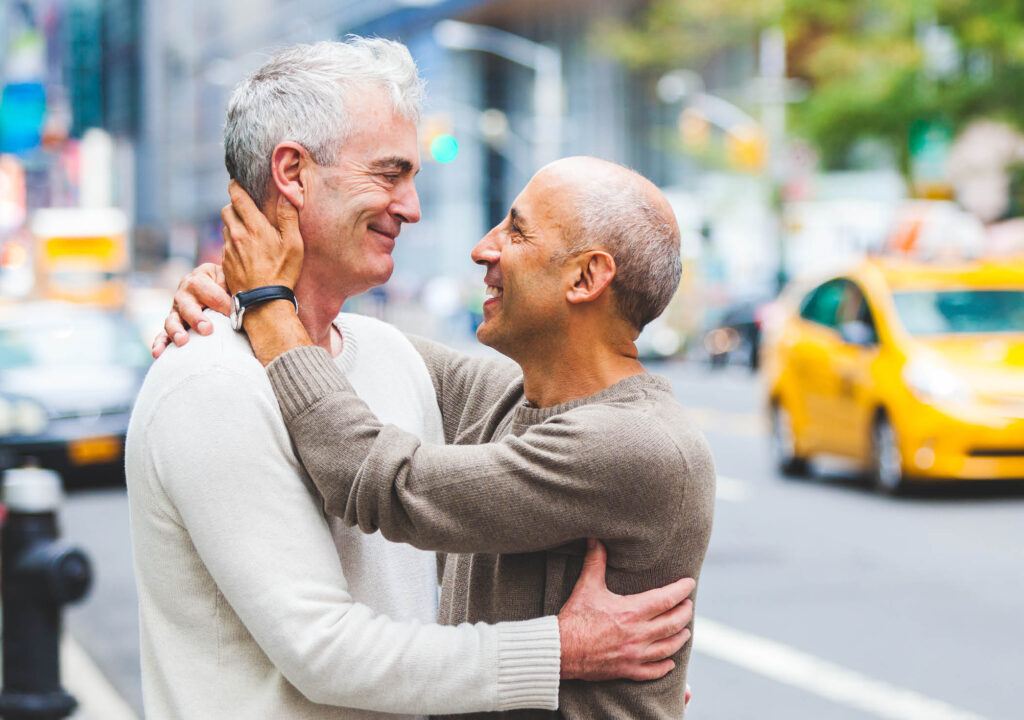 Gay couple in New York with traffic on background. Two senior men hugging and cuddling each other next to a busy street in New York city. Homosexual senior couple concept