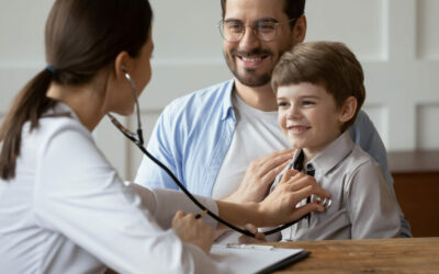 Female pediatrician listen to smiling 6s boy patient heart chest with stethoscope during visit with dad to clinic. Woman doctor examine small child at consultation with father. Healthcare concept.