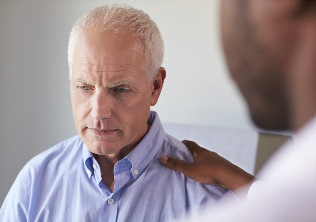 Doctor Talking To Unhappy Male Patient In Exam Room