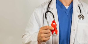 Medical professional holds a red ribbon symbolizing HIV awareness warmly. A healthcare professional with a stethoscope wears a white coat and blue scrubs, holding a red ribbon that represents HIV awareness and support during a health awareness campaign.