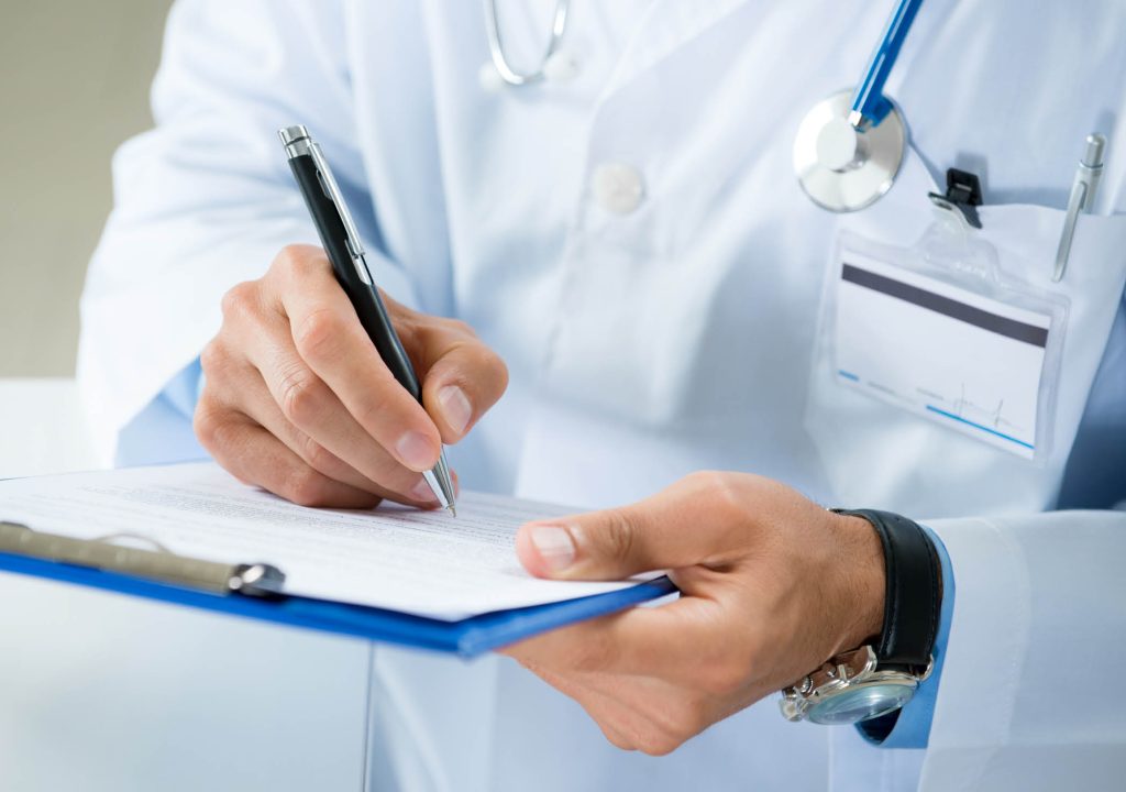 Male Doctor Writing On Medical Document. Close-up Of Male Doctor Filling The Medical Form
