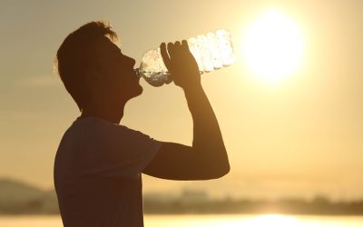 Profile of a fitness man silhouette drinking water from a bottle at sunset with the sun in the background