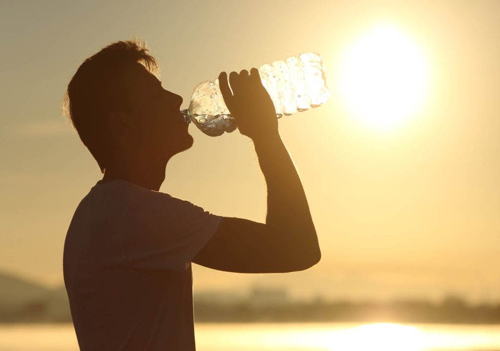 Profile of a fitness man silhouette drinking water from a bottle at sunset with the sun in the background