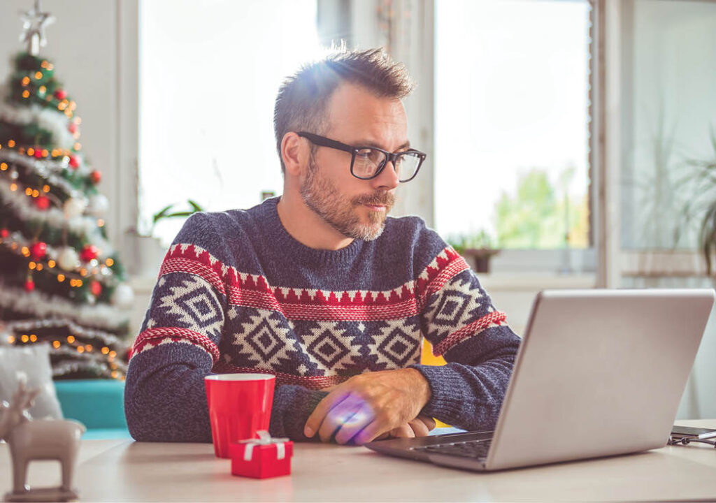 Men wearing blue sweater and eyeglasses using laptop_Christmas holidays