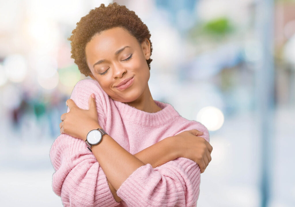 Beautiful young african american woman over isolated background Hugging oneself happy and positive, smiling