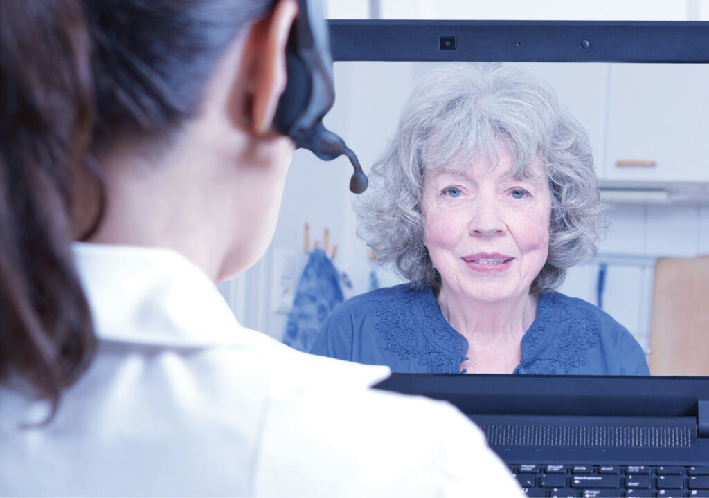 Female doctor of geriatrics with headset in front of her laptop during an consultation over the internet with a senior patient, telemedicine concept