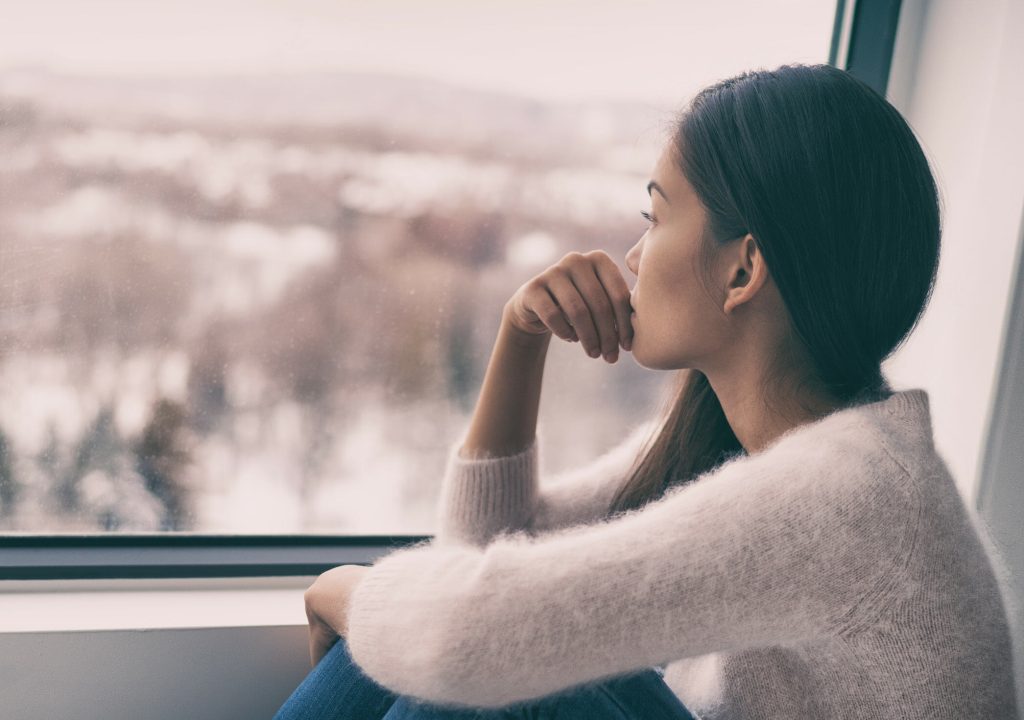 Sad pensive woman at home Winter depression - seasonal affective disorder mental health looking out the window alone. Self isolation