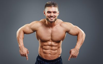 Smiling muscular man pointing down. Half body studio shot isolated on grey