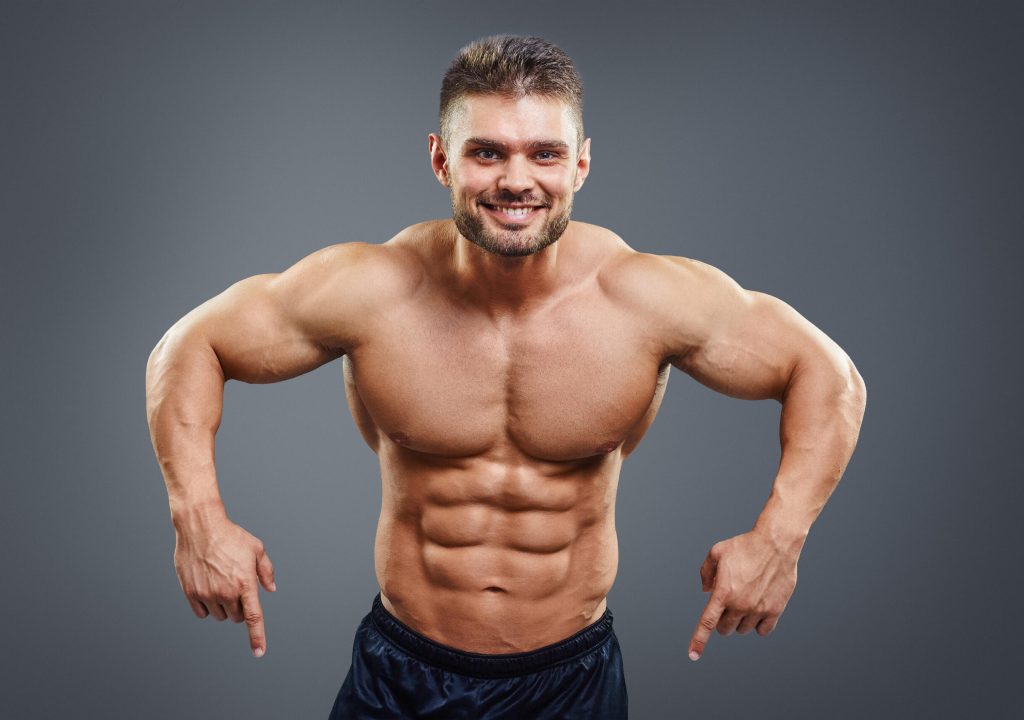 Smiling muscular man pointing down. Half body studio shot isolated on grey
