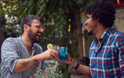Two young multiethnic male laughing and toast with cocktails in outdoor cafe. multiethnic, friendship, socializing, leisure, casual