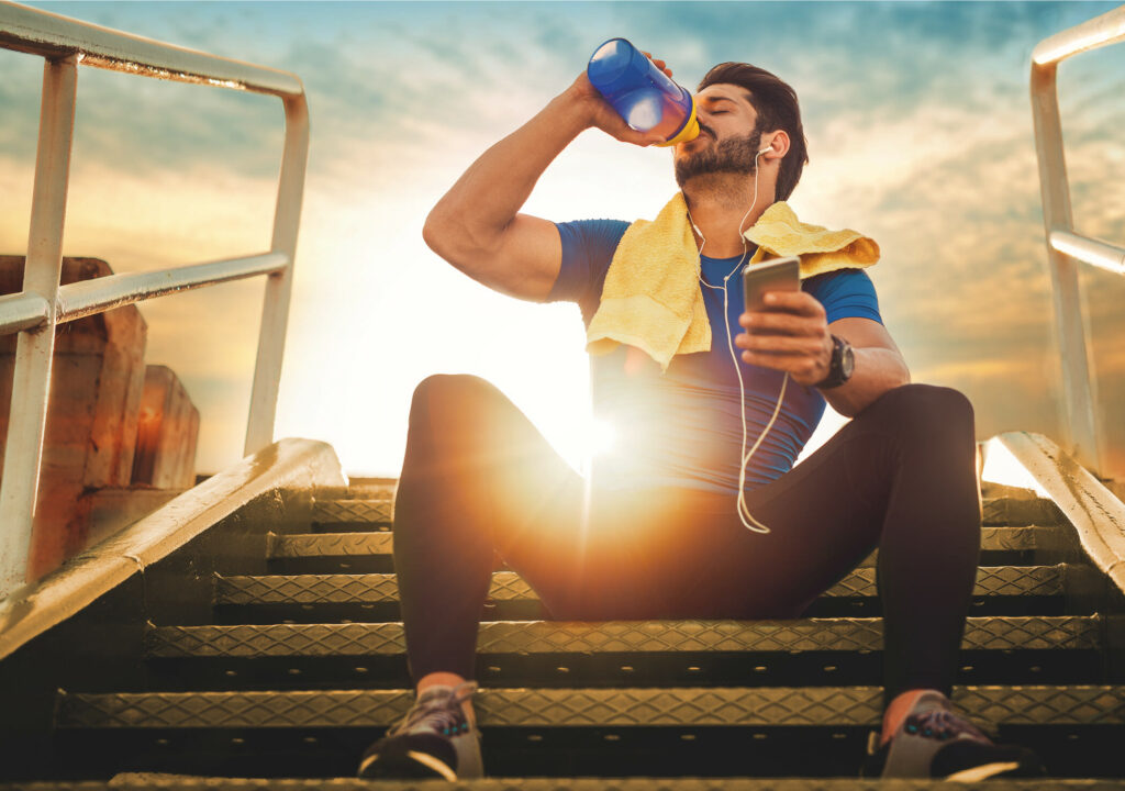 athletic man sitting on stairs and drinking water