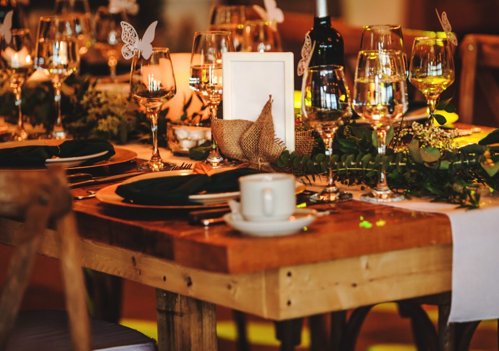 Elegant arrangement of the holiday tableware. Vintage decoration of reception dinner table. Rustic wedding table setting in fancy American restaurant. Wine glasses, plates, forks and green briefcases for the banquet