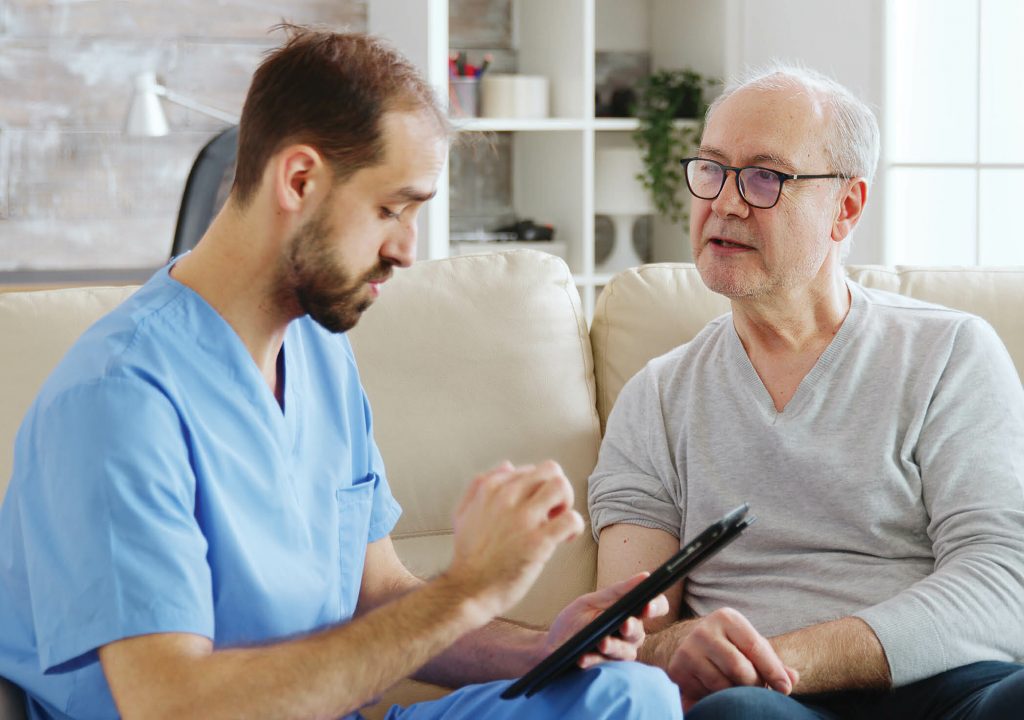 Caucasian male nurse talking with a nursing home patient about his health. The nurse is making notes on a digital tablet