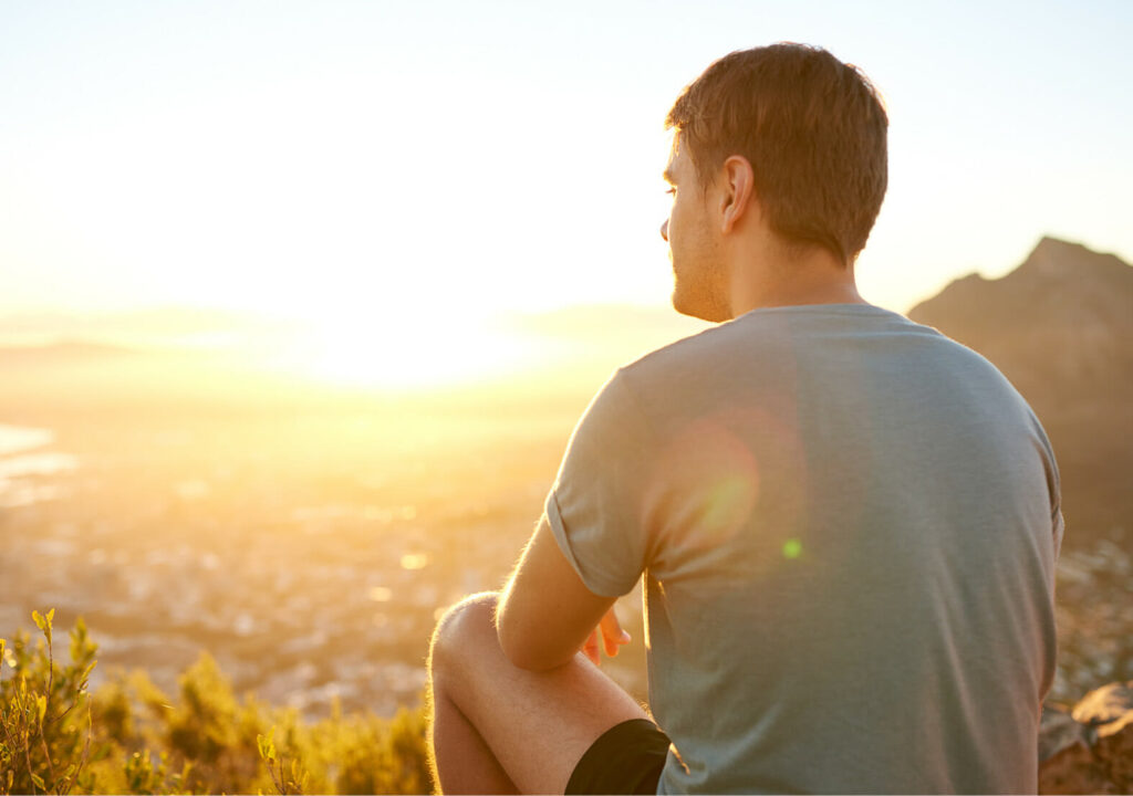 Rear view of a young guy resting on a nature trail watching the sunrise