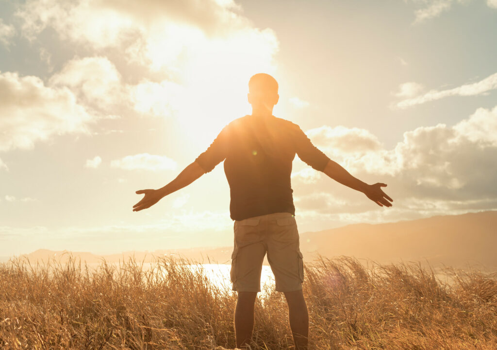 Young man feeing happy outdoors standing on a mountain taking in the warm rays of sunshine. Freedom, and happiness concept.
