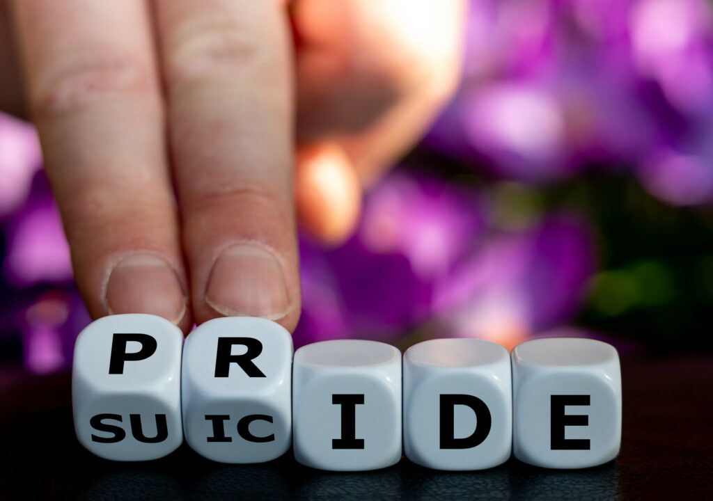 Symbol for LGBTQ mental health and suicide prevention. Hand turns dice and changes the word "suicide" to "pride".