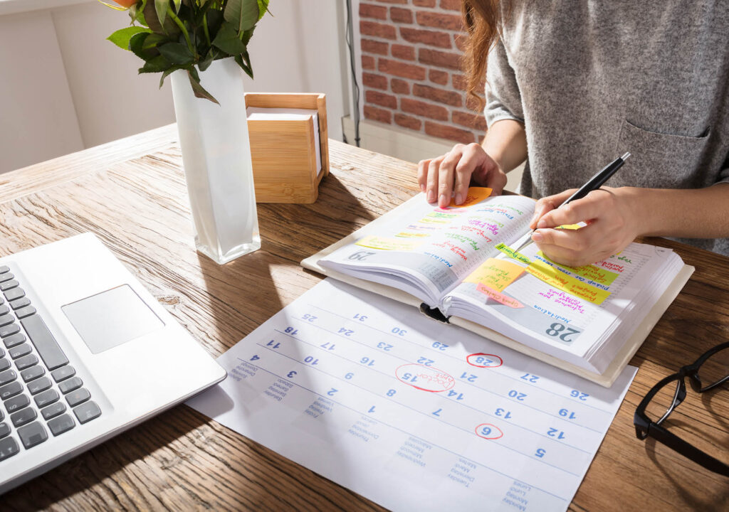Close-up Of A Businesswoman Making Agenda On Personal Organizer At Workplace