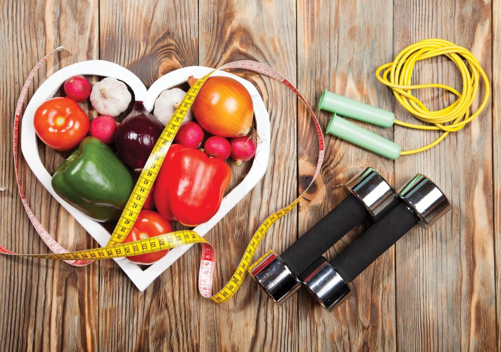 Sport and diet. Vegetables, dumbbells and centimeter. Peppers, tomatoes, garlic, onions, and radishes in the heart on rustic background