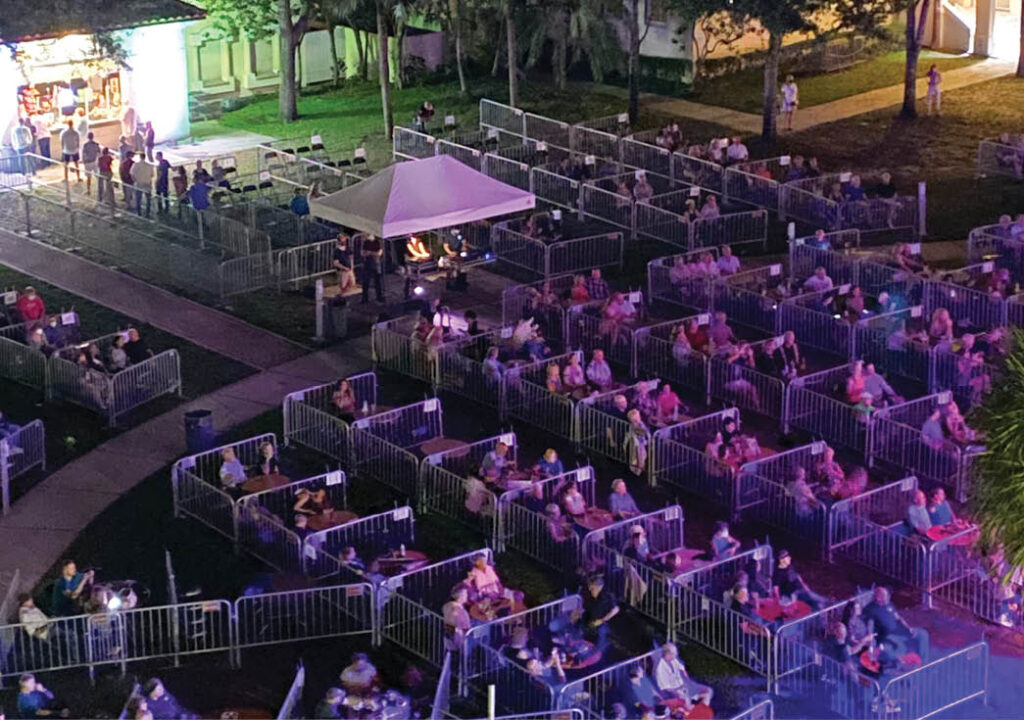 People seating outside in front of the stage in socially distanced pods.