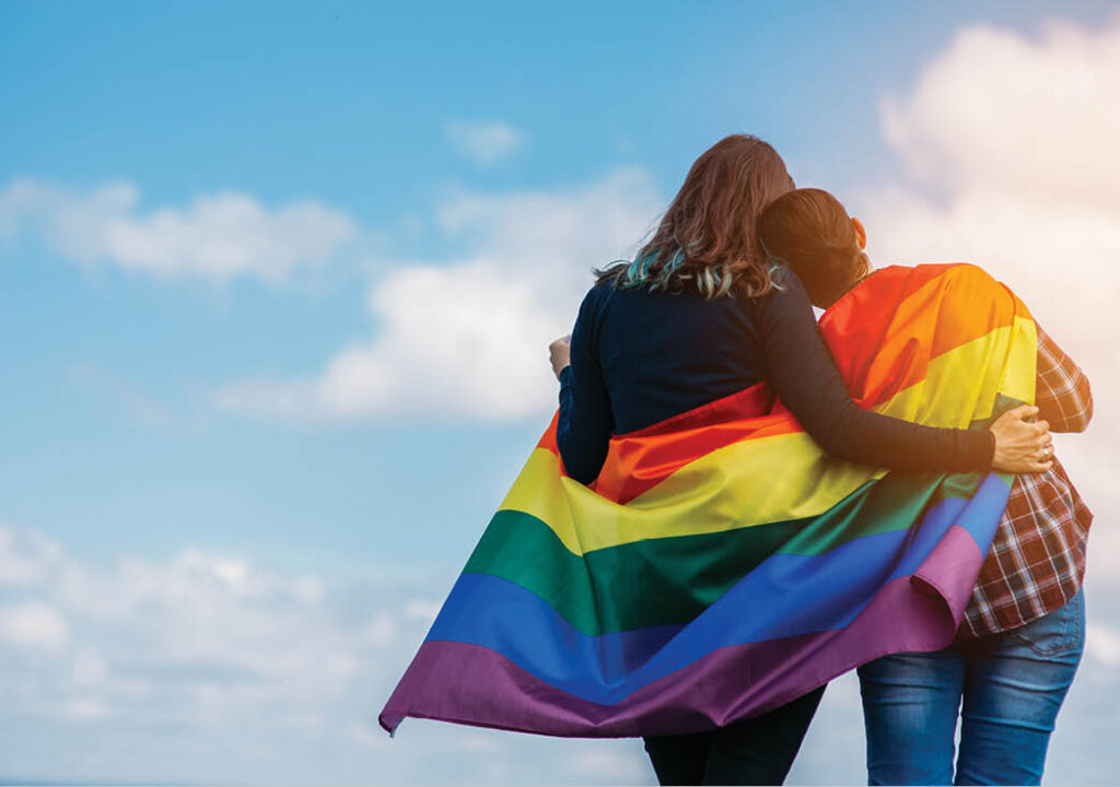 Lesbian couple hugging outdoors. LGBT rainbow flag
