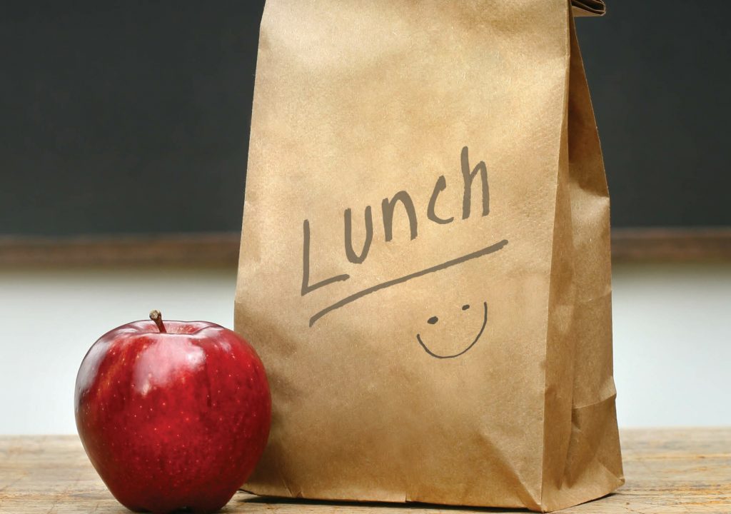 Paper lunch bag on desk with apple