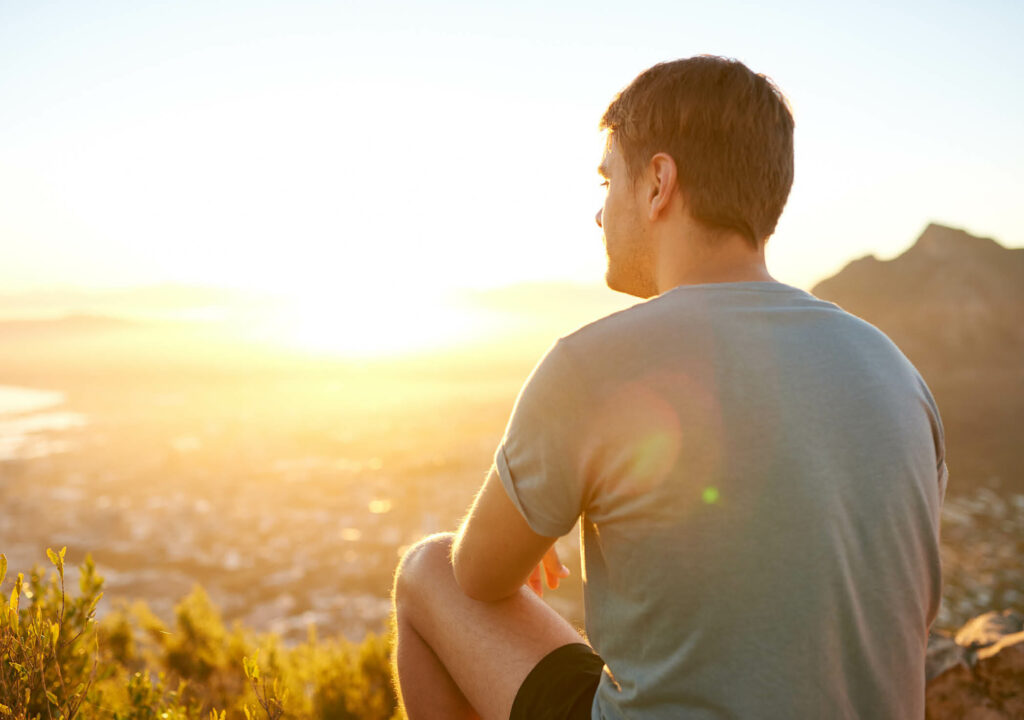 Rear view of a young guy resting on a nature trail watching the sunrise