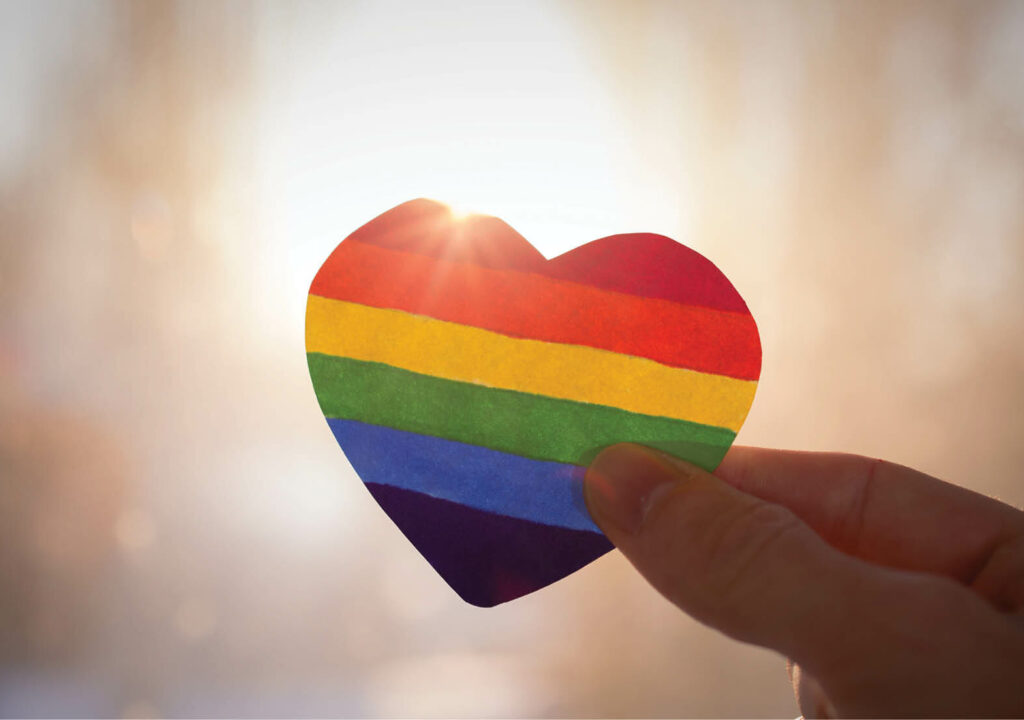 lgbt rights concept, hand holds a heart painted like a LGBT flag, silhouetted against sun