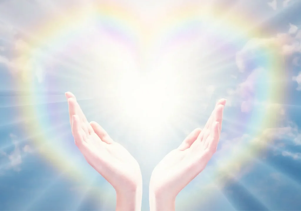 Magical love healing universal energy, rainbow heart hands. Hands holding the sun, against blue sky with clouds. Bright white light energy, bursting sun rays and rainbow heart. Magical love healing energy, dreams, wish, blessing, miracle, divine love concept.