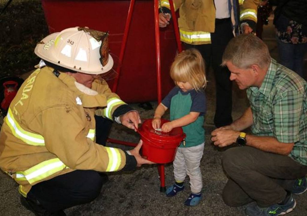 Luke Schofield (center) donates to The Salvation Army of Broward with the help of City of Fort Lauderdale Deputy Fire Chief/Fire Marshal Jeff Lucas and Robert Schofield at last year’s Christmas on Las Olas event. Photo courtesy of Goodman PR